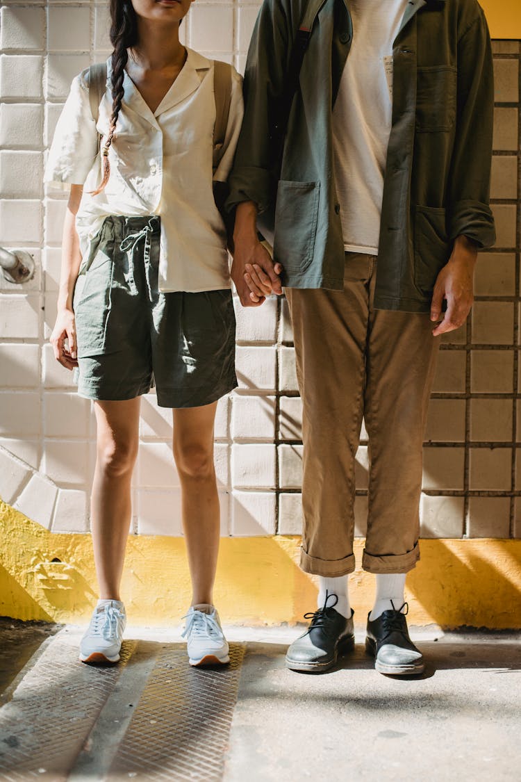 Anonymous Stylish Couple Holding Hands Near Wall In Subway Station