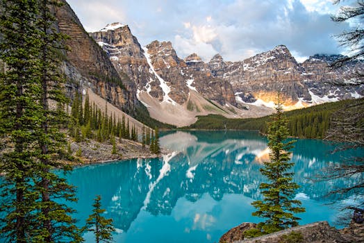 Breathtaking view of Moraine Lake with reflection of snow-covered mountains, pine trees, and vibrant blue water.