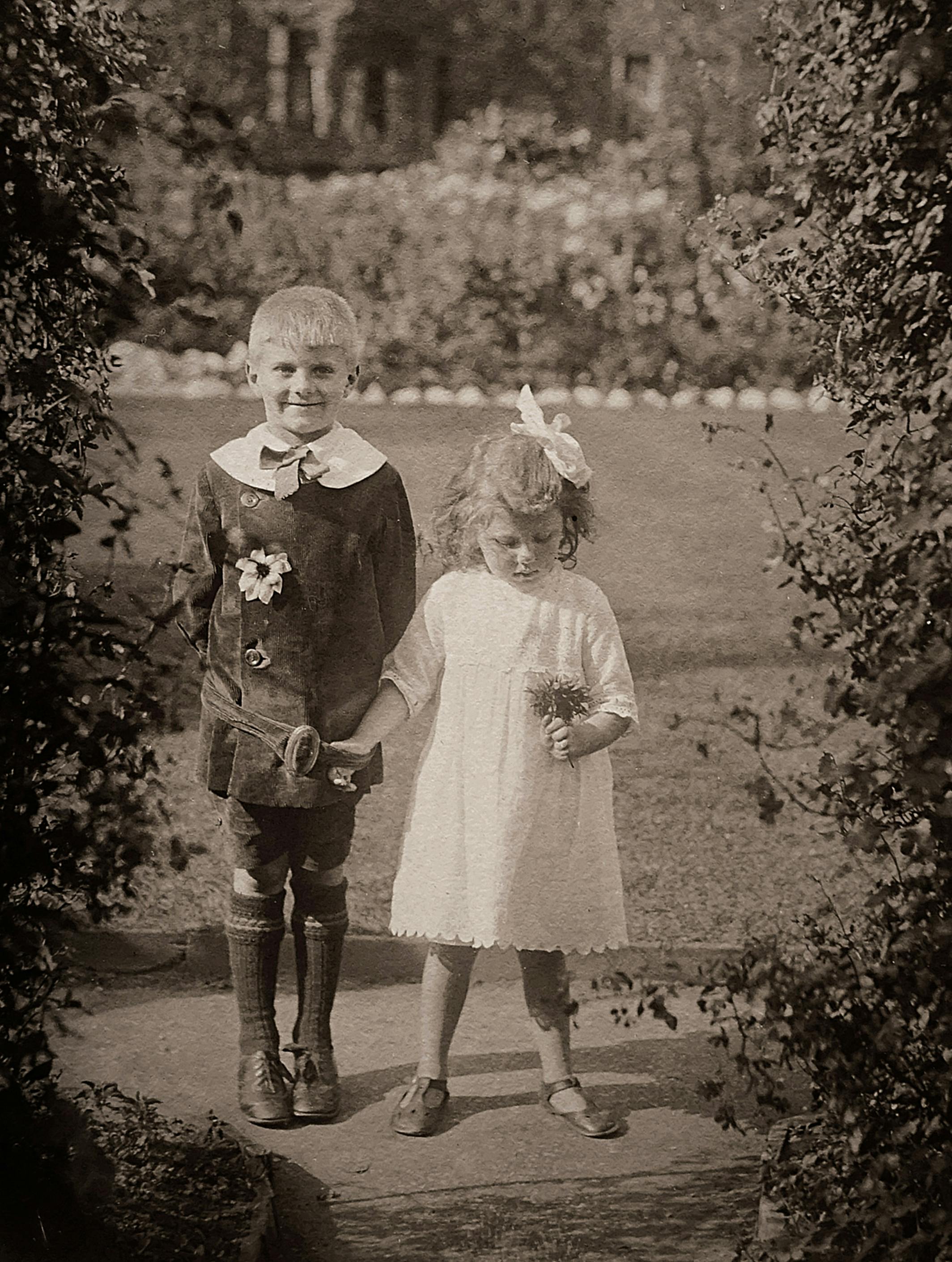 Charming vintage photo of a brother and sister holding hands in a garden.