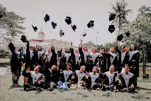 People in Blue Academic Dress Sitting on Green Grass Field