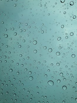 Raindrops on glass window with a serene sky backdrop, capturing nature's patterns.