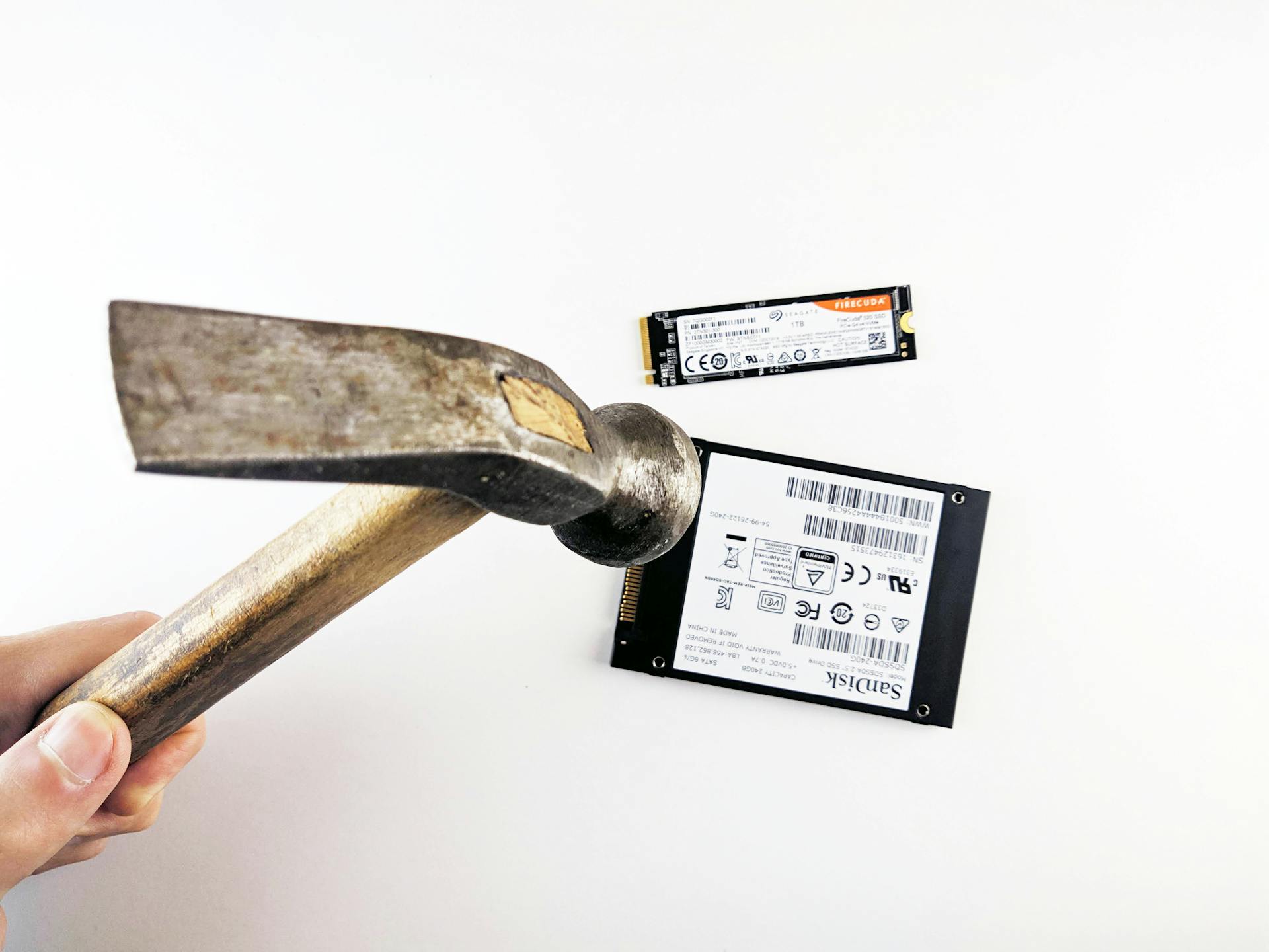 Close-up image of a hammer poised to strike a hard drive and SSD, symbolizing data destruction.