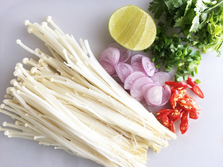 Frasco de ajvar rojo al lado de un puñado de champiñones enoki frescos sobre fondo blanco