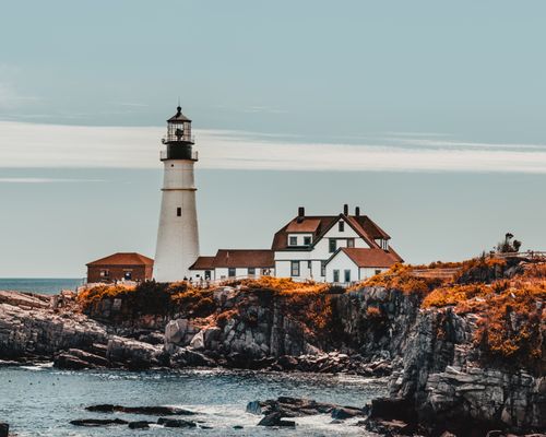Free Lighthouse near big house near orange grass on rocky shore near ocean under bright sky in daytime Stock Photo