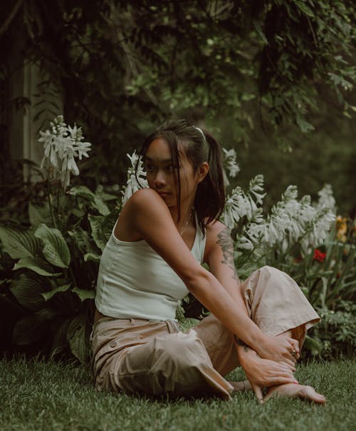 Full body of calm young Asian female resting in green park and sitting with crossed legs