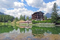 Brown Wooden House Near Green Trees and Lake Under Blue Sky and White Clouds