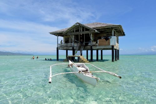 Free Serene tropical seascape with overwater cottage and outrigger boat in clear waters. Stock Photo