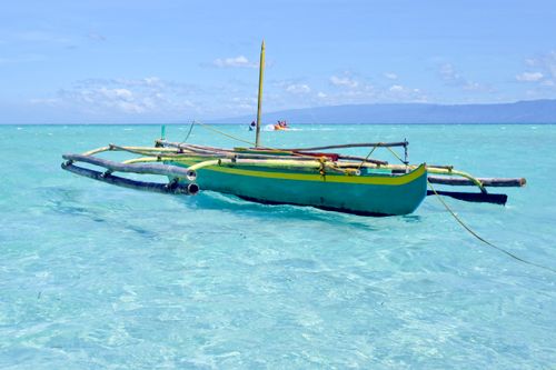 Free A vibrant outrigger canoe floats on pristine turquoise waters under a sunny sky. Stock Photo