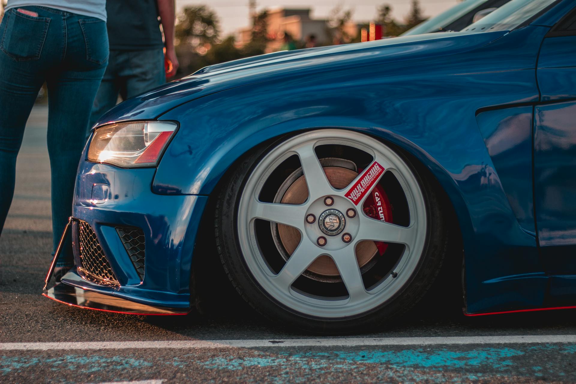 Crop anonymous people standing near stylish shiny blue sports car with tuned bumper and rims parked on street in sunlight