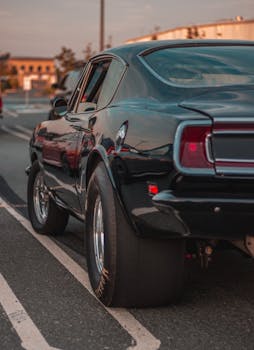 Rear view of a classic black car parked on a street at sunset, showcasing its vintage design.
