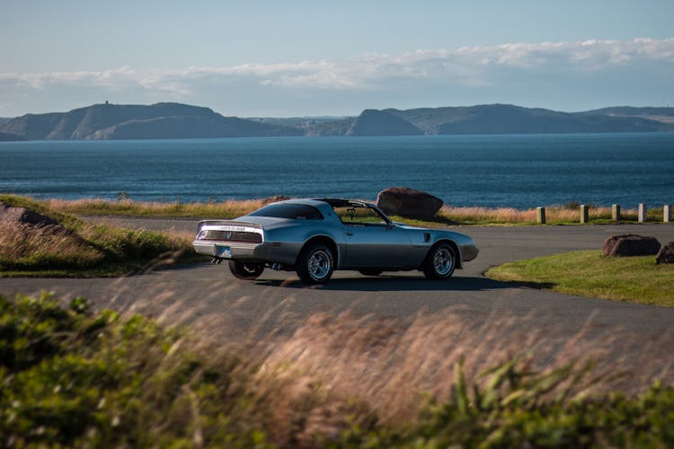 Retro Sports Car On Paved Road Near Lake And Valley In Daytime