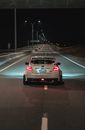 Expensive white tuned sports car riding on even paved road under black sky in light of lamps