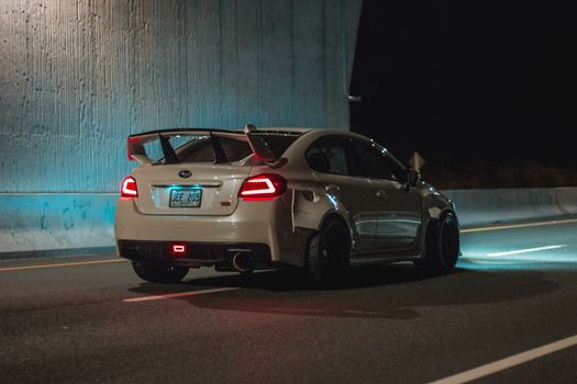 Sports car riding on road under bridge at night