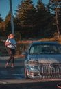 Focused young slender female worker washing automobile parked on pavement next to lush dark green woodland under blue cloudless sky in evening