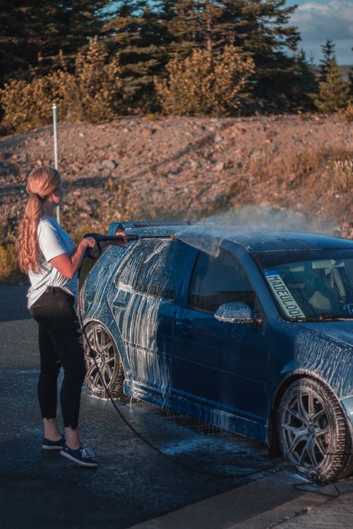 Free Full body side view unrecognizable slender female worker in casual clothing using hosepipe while cleaning automobile at car wash in daylight Stock Photo