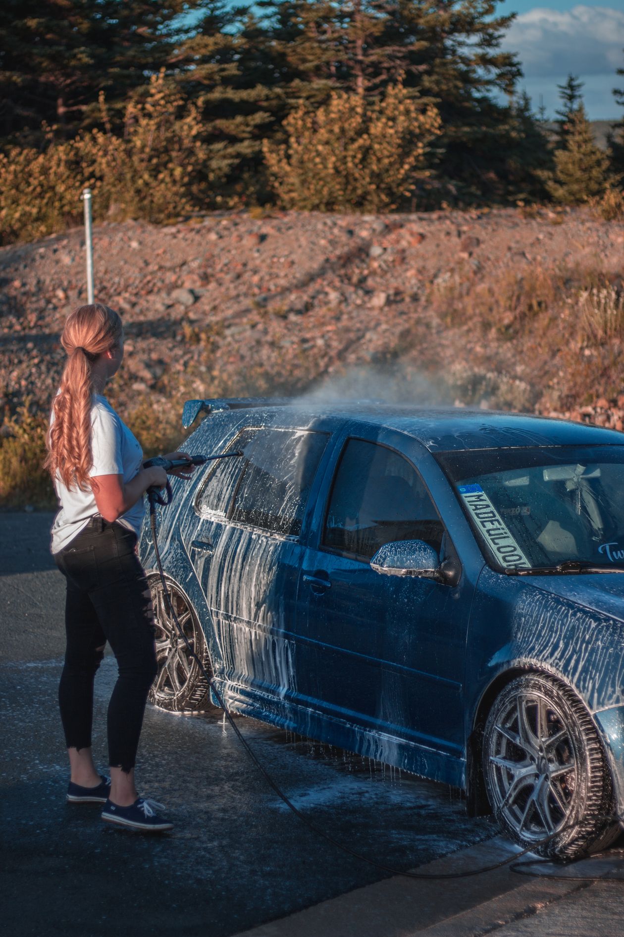 Team member rinsing a car with a hose in bright daylight