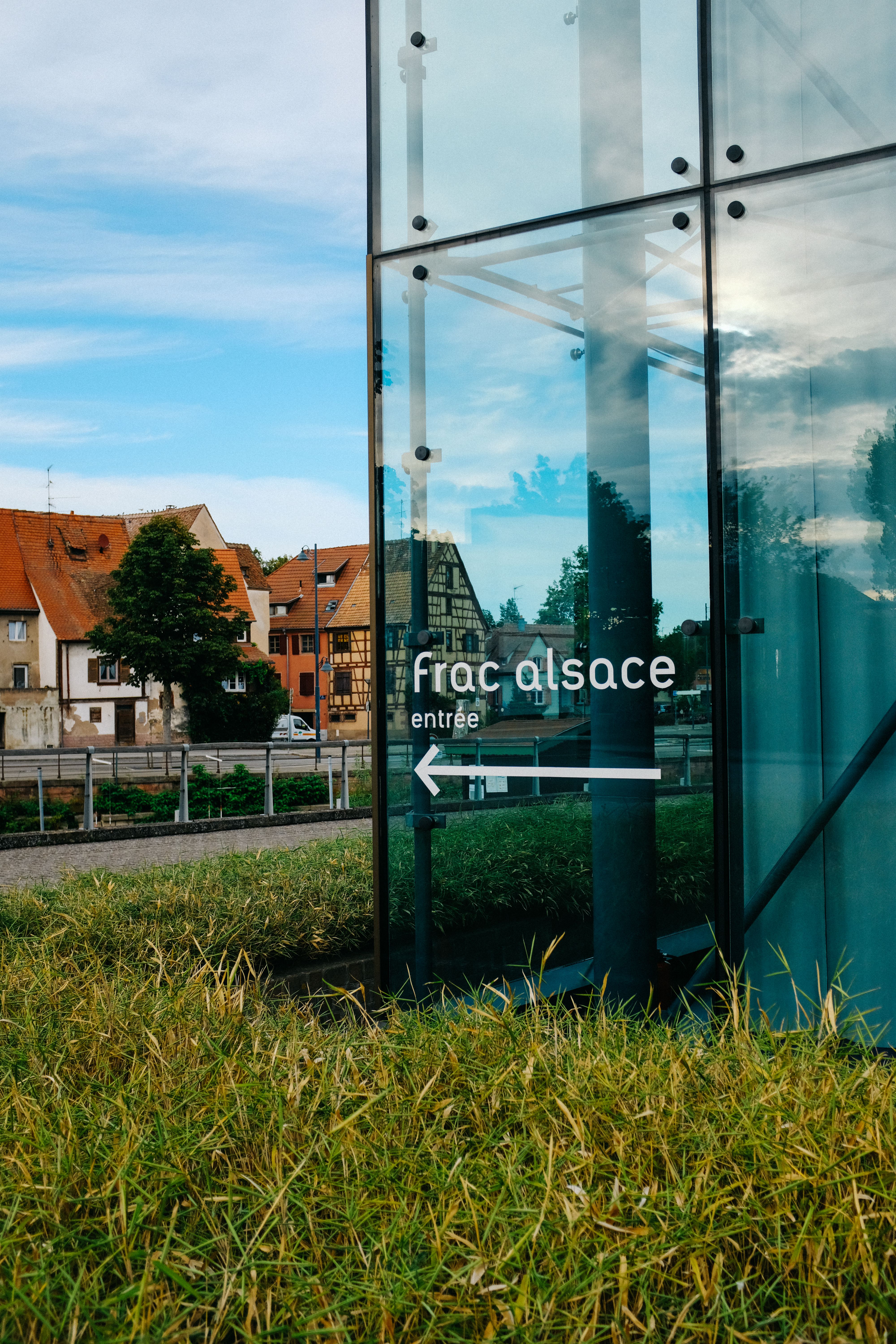 Contemporary glass building wall with guiding white inscription and arrow located in suburb on summer day