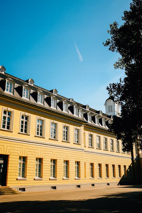 Yellow facade of long historic building with ornamental walls and spire under clear blue sky