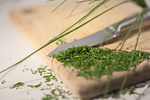Close-up of fresh chives being chopped on a wooden board with a knife. Ideal for culinary themes.