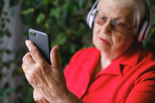 Free A Man in Red Shirt Using a Phone while Wearing Headphones Stock Photo