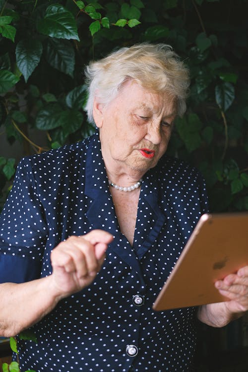 Free Aged smart female working online and surfing internet while using tablet in garden Stock Photo