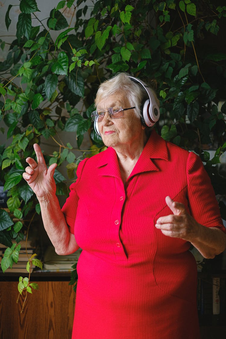 Senior Happy Woman In Red Dress And Headphones Dancing