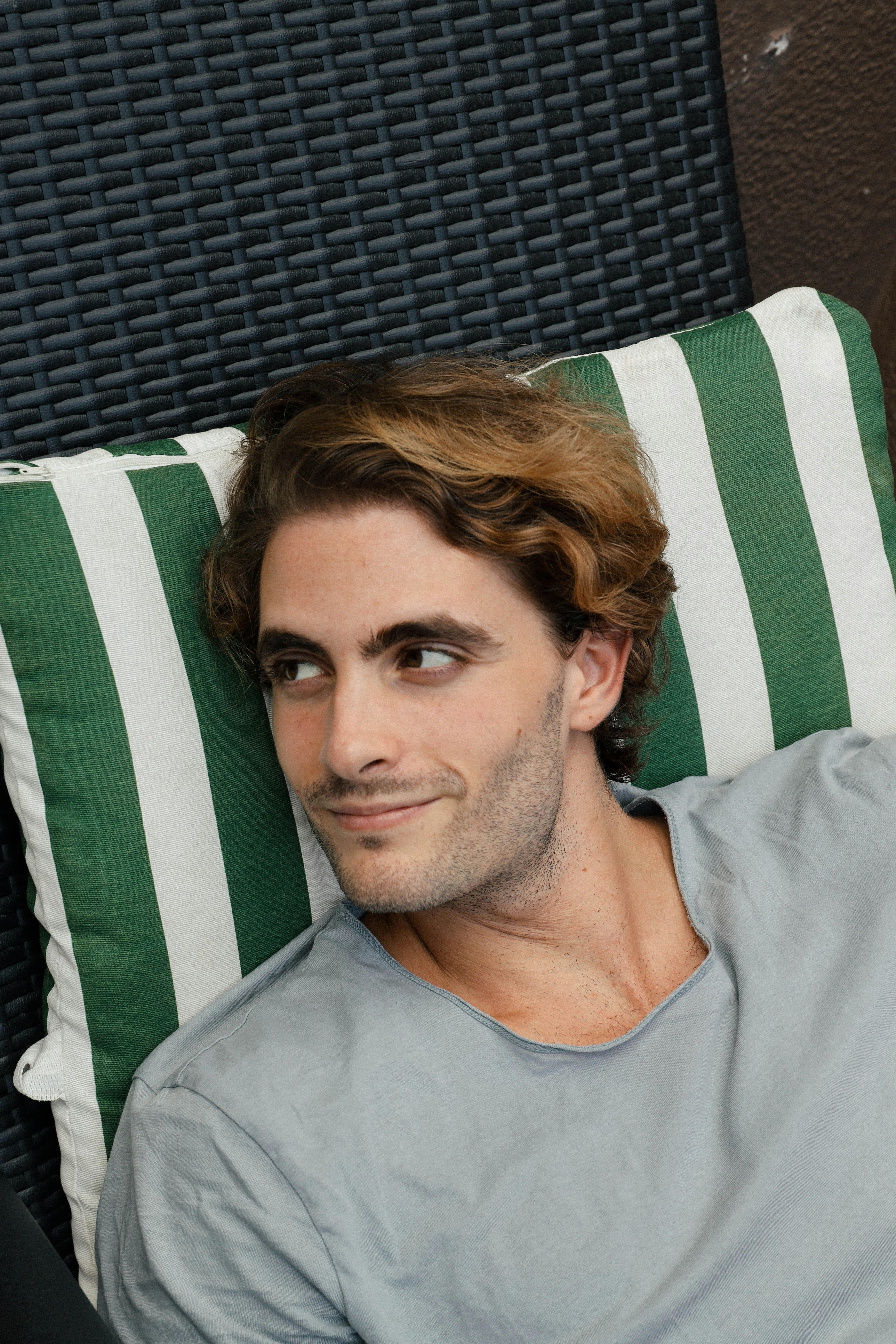 A relaxed young man smiles while lying on a striped pillow outdoors. Ideal for lifestyle themes.