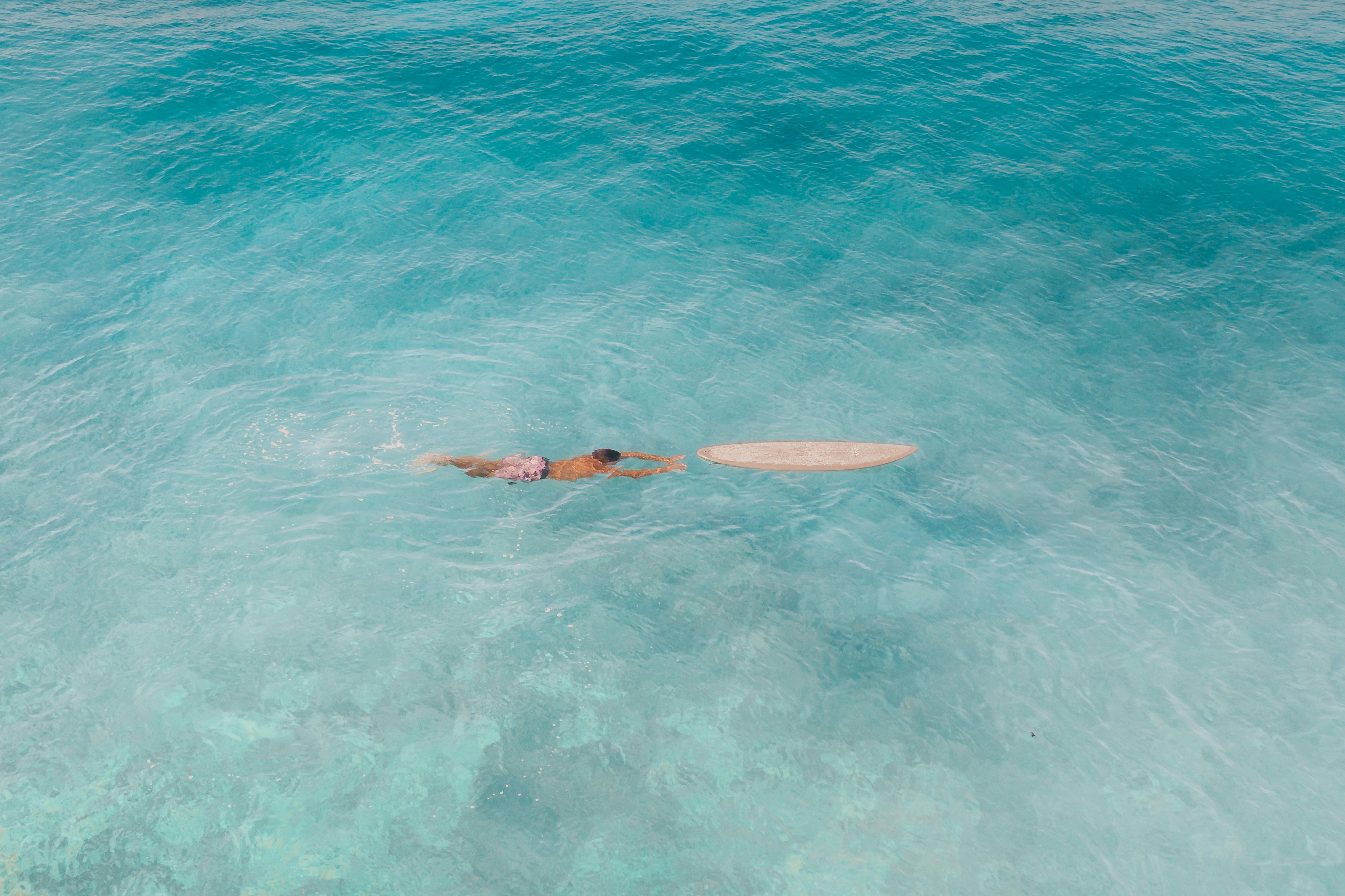 从上面看，一名冲浪者正漂浮在冲浪板旁，周围是平静、清澈的碧绿海水