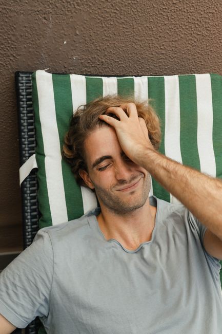 A young man with closed eyes relaxes on a striped sunbed outdoors, enjoying a moment of peace.