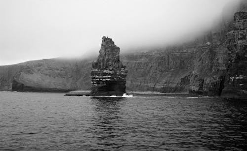 Grayscale Photo of Rock Formation on Body of Water