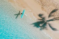 空中拍摄的一个冲浪者走在一个热带海滩与绿松石水和棕榈阴影