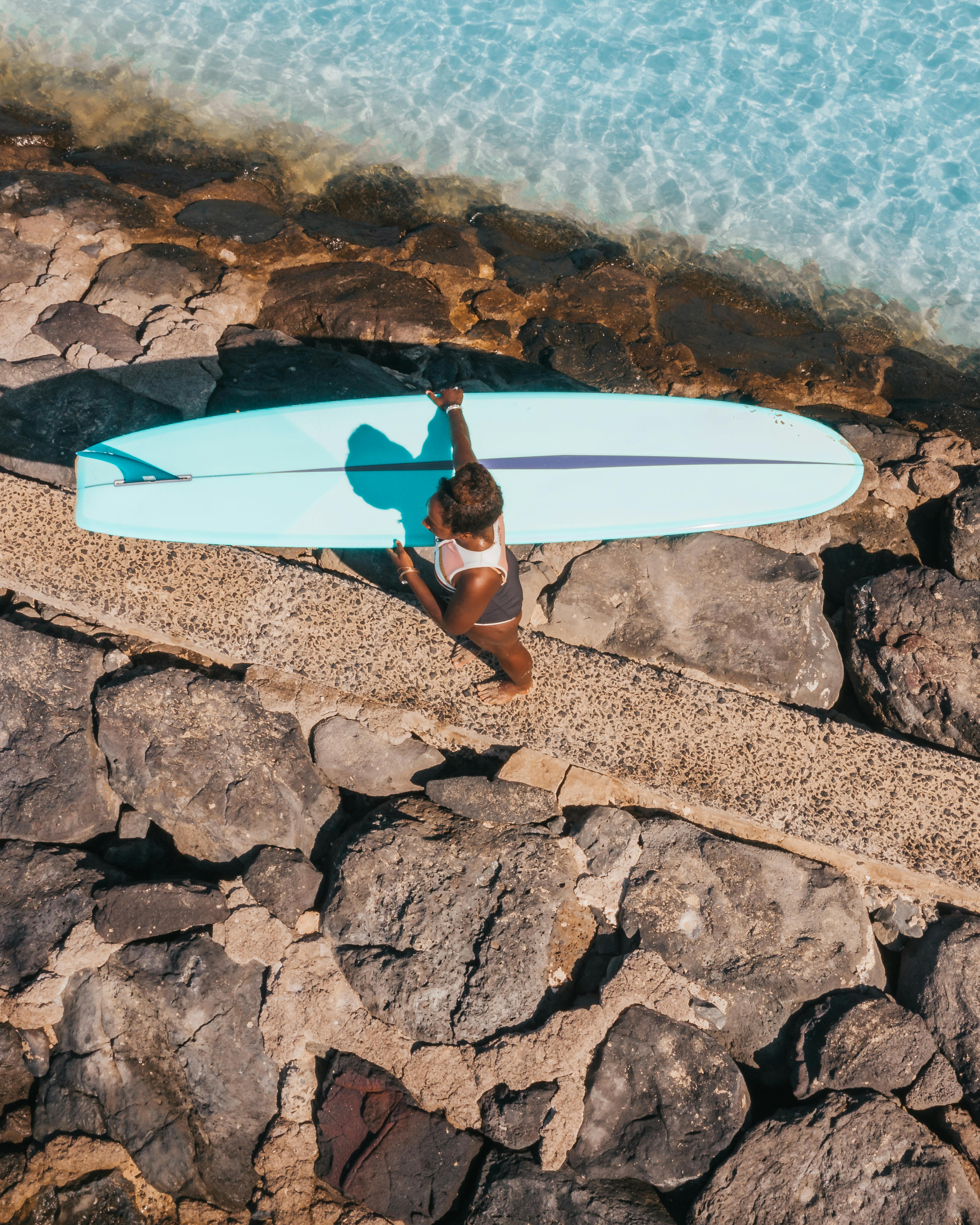在阳光明媚的环境中，冲浪者沿着岩石小径行走，他们的冲浪板靠近水