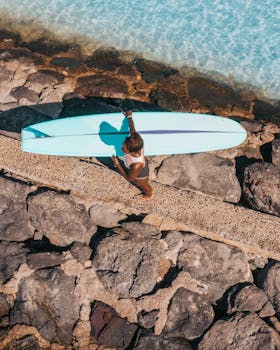 一名冲浪者带着冲浪板，沿着水边的岩石小路，在明媚的阳光下行走