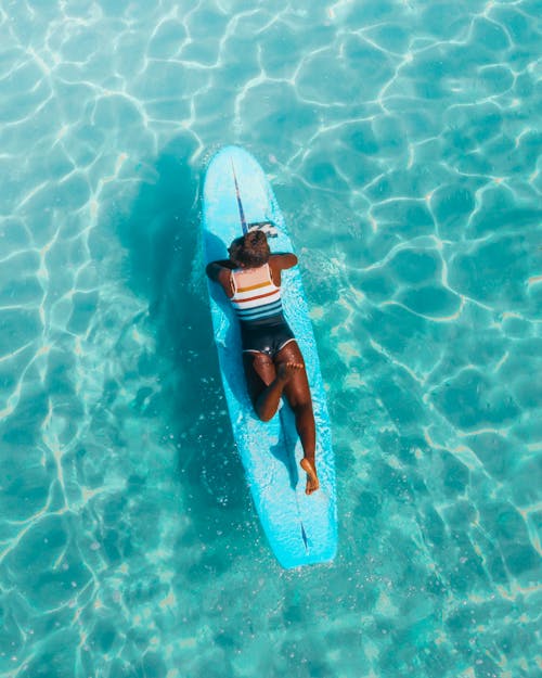 A Woman Lying on Blue Surfboard on the Sea