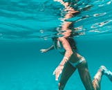 一名女子在清澈蔚蓝的大海中游泳，阳光反射在水面上