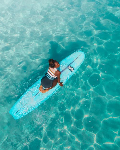 Free Aerial shot of a woman on a surfboard in clear, turquoise water, conveying a sense of adventure and tranquility. Stock Photo