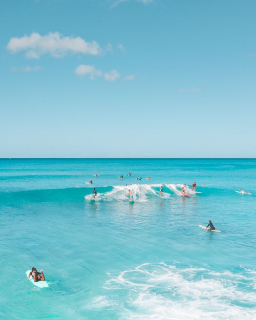 Free Energetic surfers enjoy the clear turquoise waves under a bright blue sky, capturing summer's essence. Stock Photo