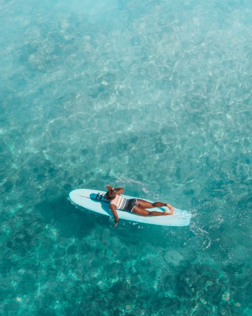 Free Tranquil aerial shot of woman on surfboard in turquoise waters, enjoying a sunny day outdoors. Stock Photo