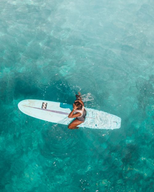 Free Aerial shot of a woman relaxing on a surfboard in clear turquoise ocean water. Stock Photo