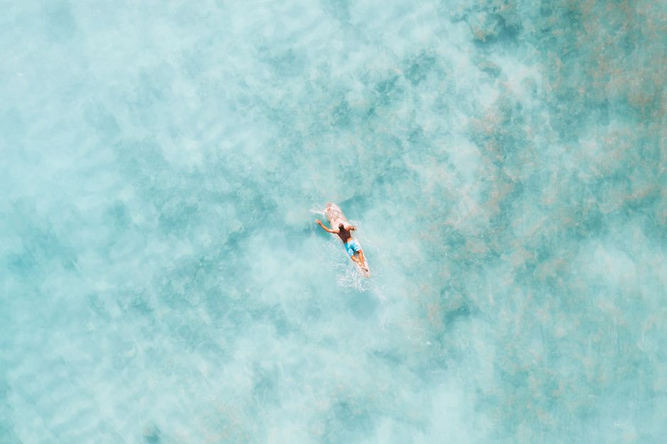 Drone shot of a surfer paddling in clear turquoise water, perfect for travel and adventure themes.