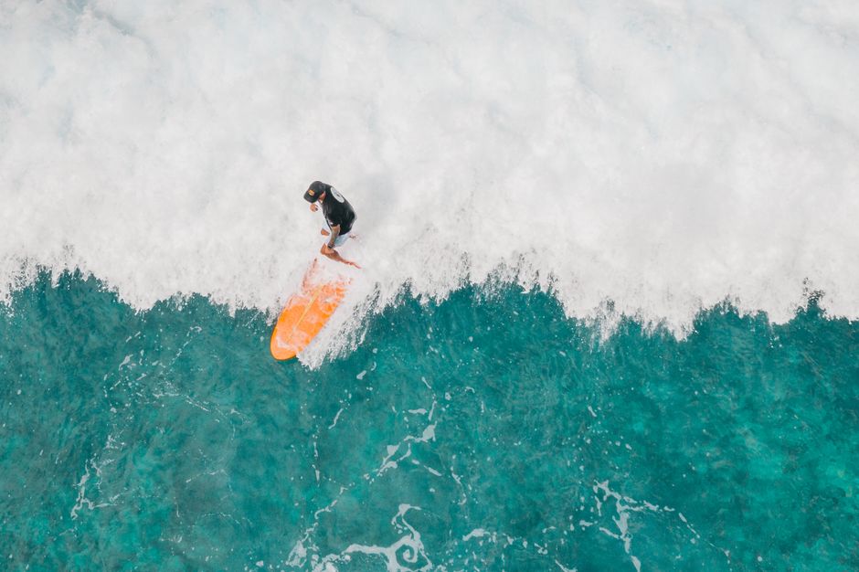 Aerial view of a surfer with an orange surfboard riding a wave in the ocean.
