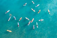 高角度拍摄的冲浪者在五颜六色的冲浪板在明确的绿松石水，从上面捕获