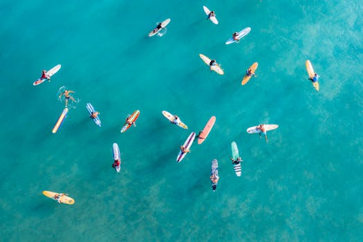 High-angle shot of surfers on colorful surfboards in clear turquoise water, captured from above.