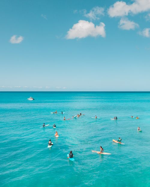 Free A stunning aerial view of surfers waiting for waves in a turquoise ocean under a bright blue sky. Stock Photo