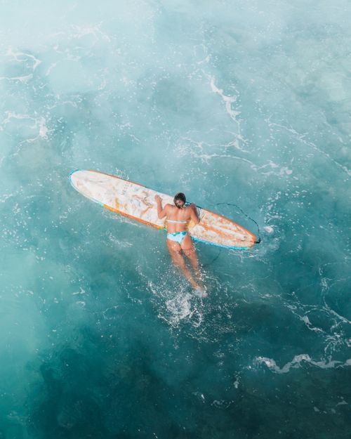 Free Woman surfing in clear blue ocean waters, showcasing a vibrant surf lifestyle. Stock Photo