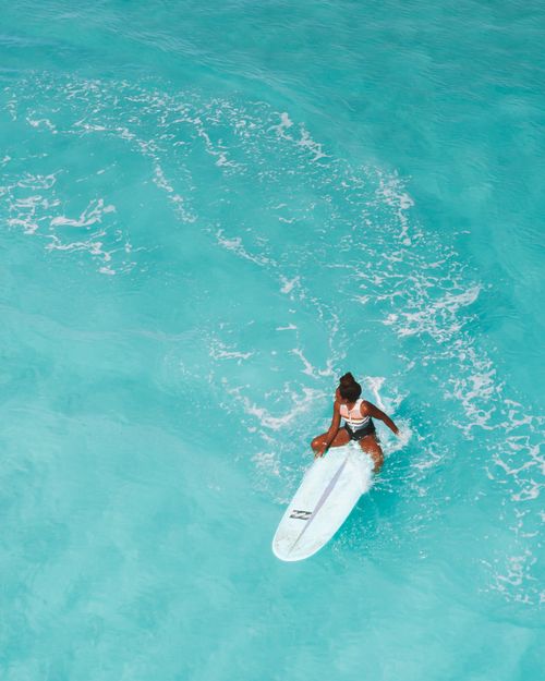Free Capture the thrill of surfing with an aerial view of a woman riding a surfboard on vibrant turquoise waters. Stock Photo