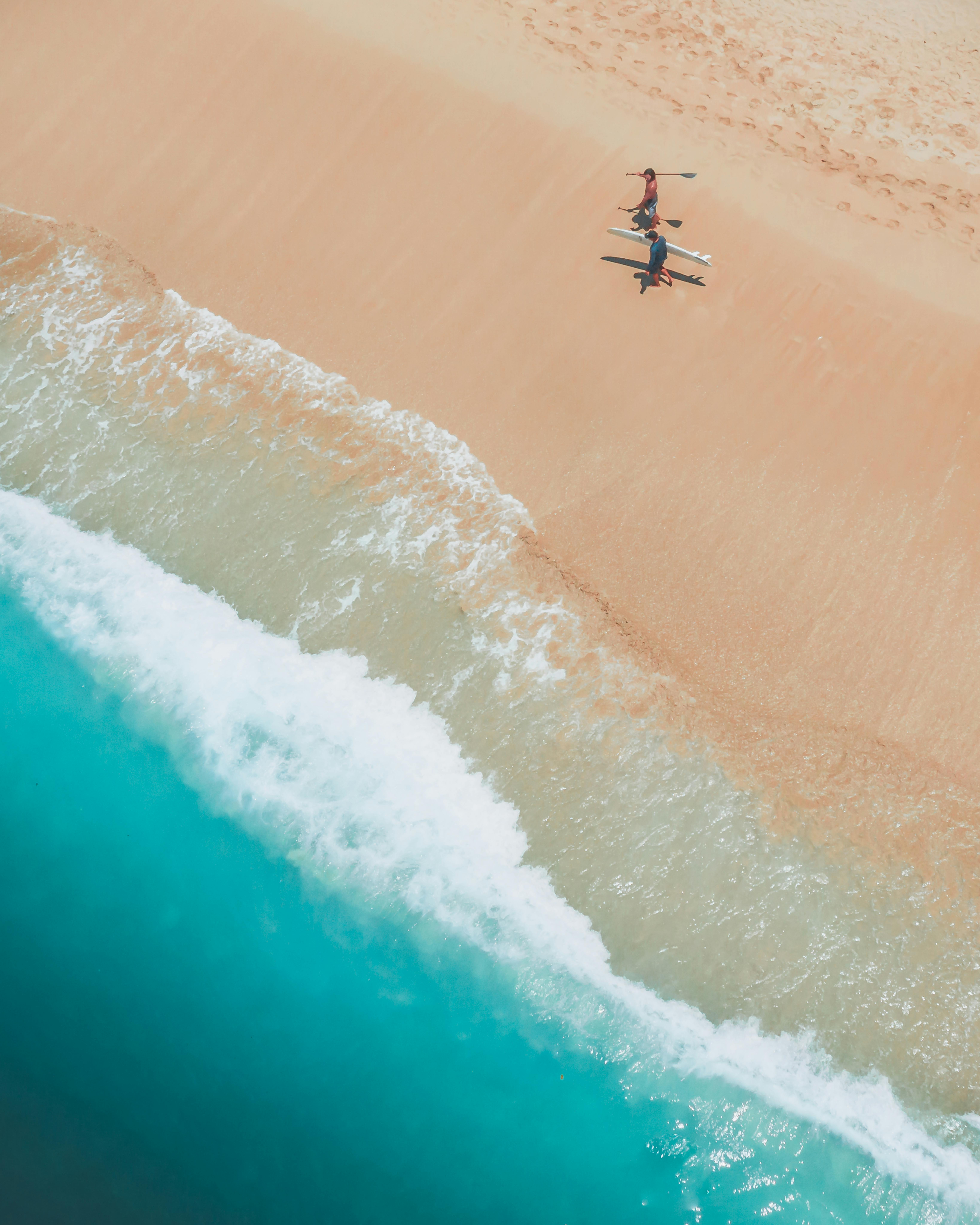 两名冲浪者从高角度观看碧绿色海浪的沙滩上行走