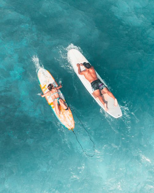 Free Vibrant aerial shot of a man and woman paddling surfboards in clear blue sea capturing the essence of water sports. Stock Photo