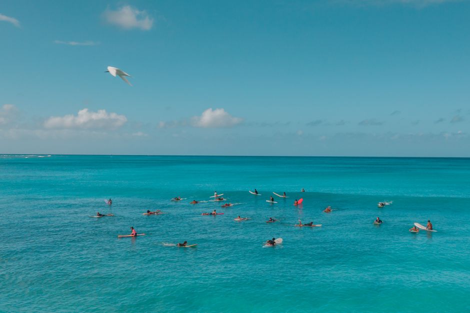 Aerial view of surfers enjoying a sunny day in the vibrant blue ocean under a clear sky.