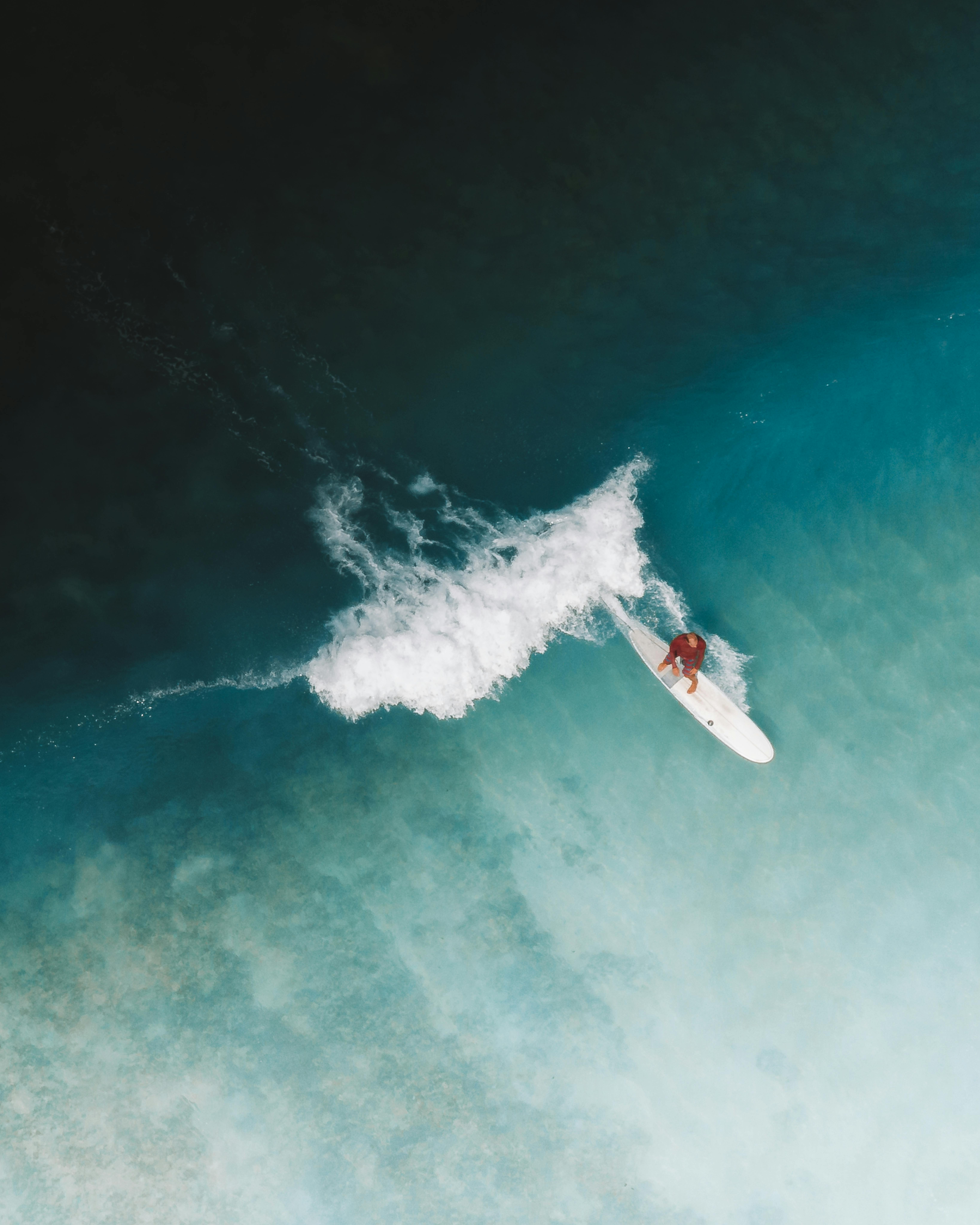 Dynamic aerial shot of a surfer navigating a wave in blue ocean waters, showcasing skill and adventure.